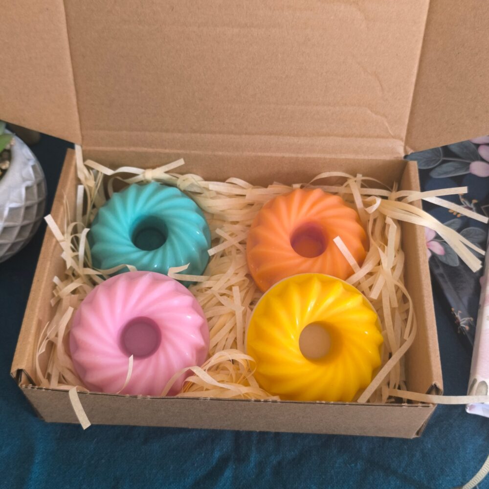 Coffret Escapade tropicale ouvert : quatre bougies moulées en forme de couronne cannelée, turquoise, orange, rose et jaune, calées dans la frisure de bois