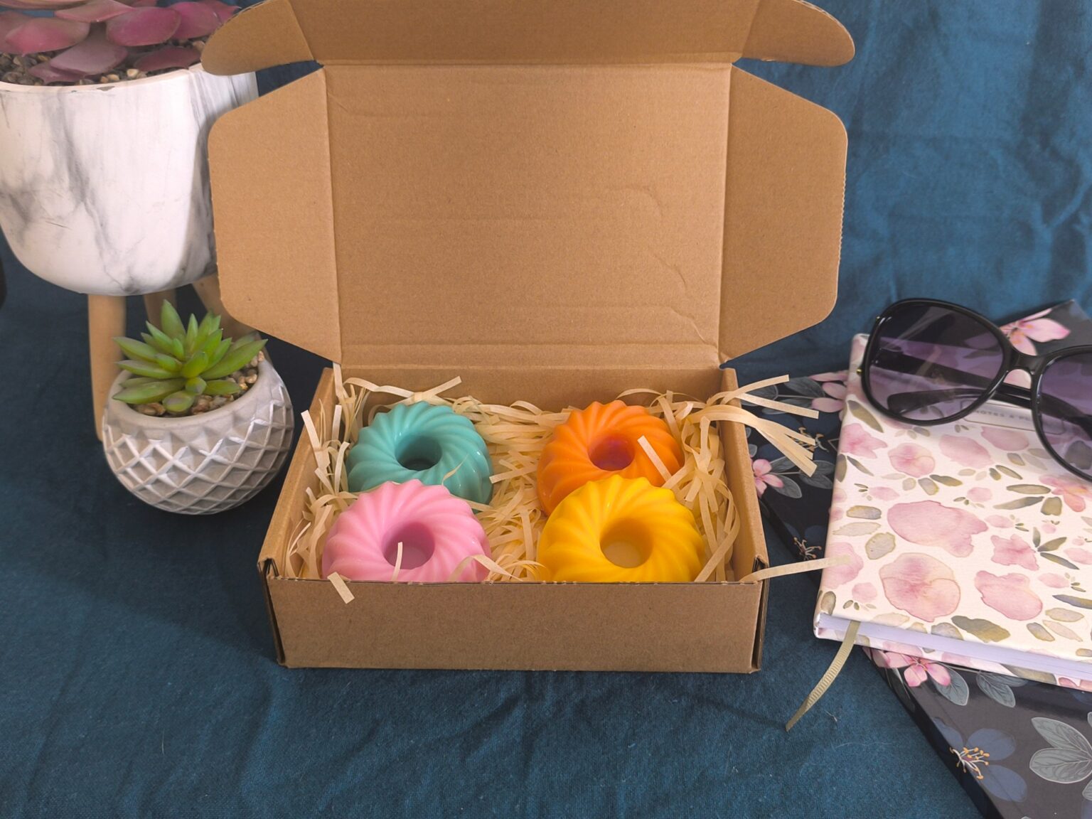 Coffret Escapade tropicale et ses quatre bougies colorées, présenté avec des plantes grasses, une pochette fleurie et des lunettes de soleil