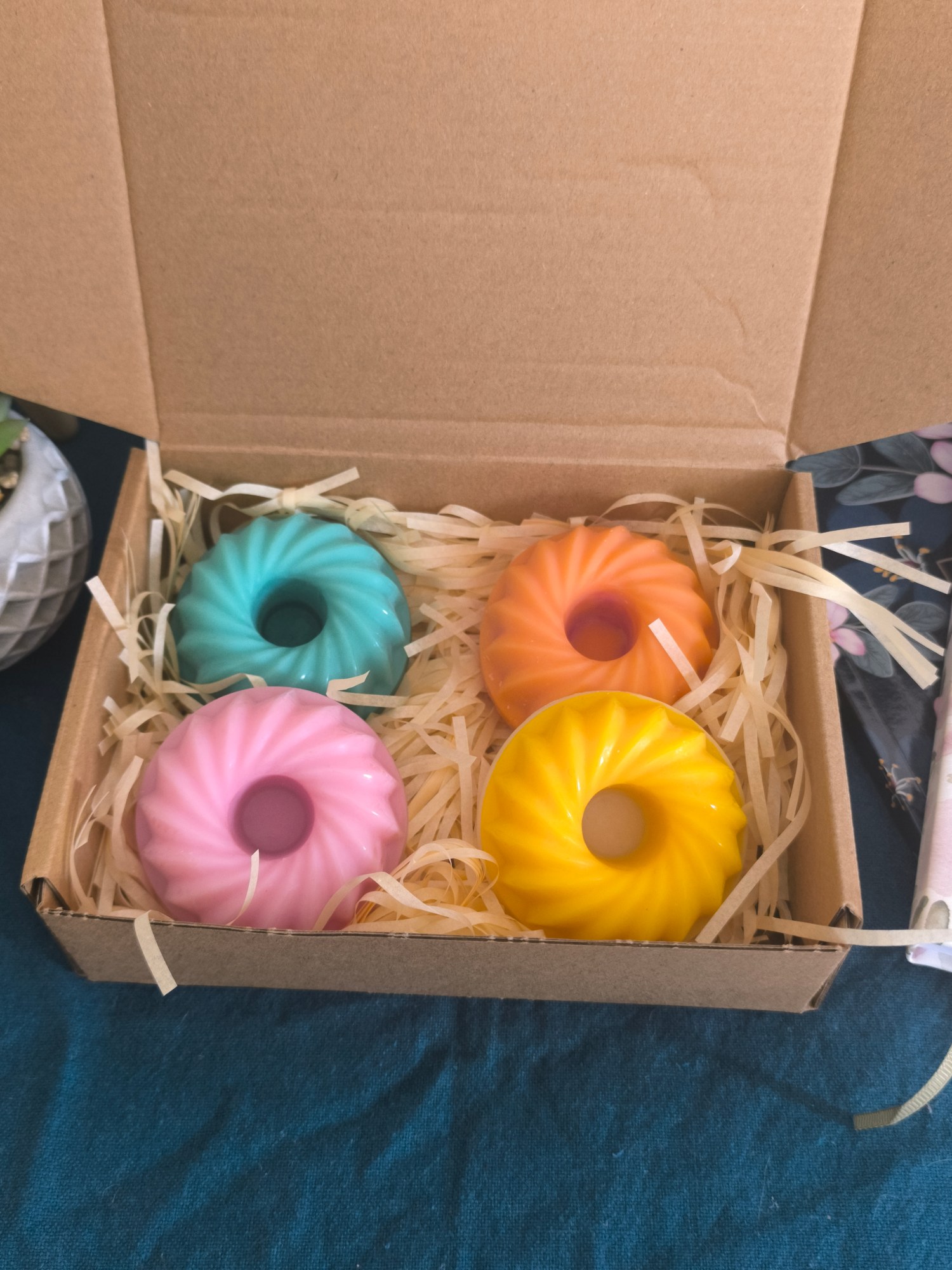 Coffret Escapade tropicale ouvert : quatre bougies moulées en forme de couronne cannelée, turquoise, orange, rose et jaune, calées dans la frisure de bois