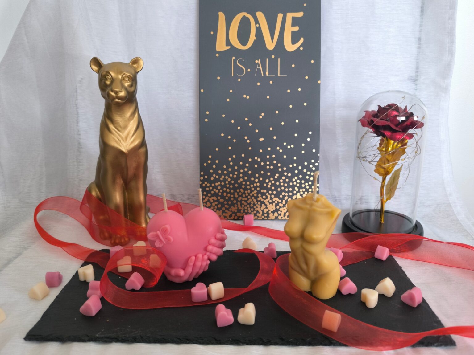 Coffret Murmure d'amour : une bougie en forme de cœur rose et une bougie buste dorée, disposées sur une ardoise avec une rose éternelle sous cloche