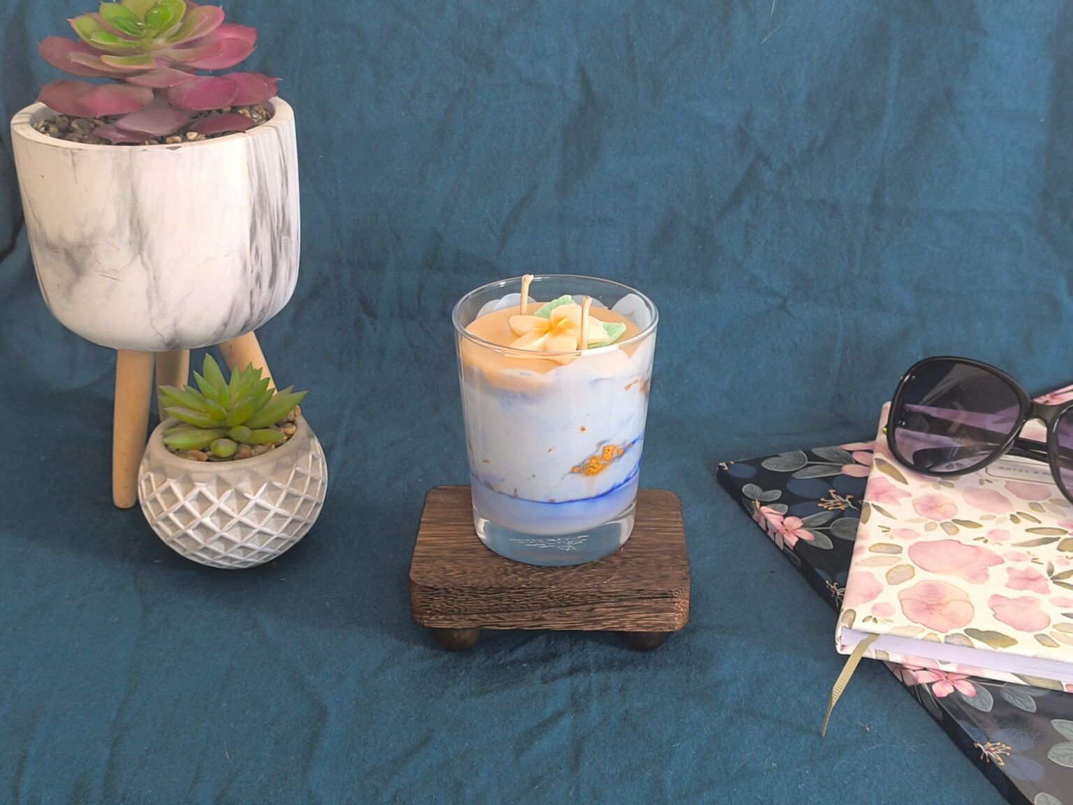 Bougie Rêve Polynésien en décor estival, entre deux plantes grasses, une pochette fleurie et une paire de lunettes de soleil